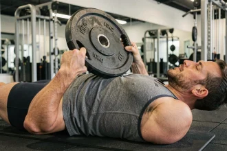 Homme effectuant un crunch avec poids en salle de sport, abdominaux contractés tenant une plaque de musculation sur la poitrine