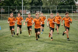 Jeunes joueurs de football en maillot orange courant sur le terrain d'entraînement du Sporting Club Aubagne Air Bel