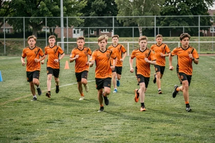 Jeunes joueurs de football en maillot orange courant sur le terrain d'entraînement du Sporting Club Aubagne Air Bel
